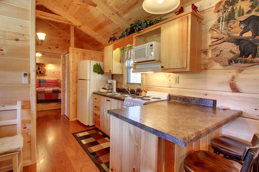 Cabin interior with stone countertops, stove and oven, microwave, sink, coffeemaker, and bed