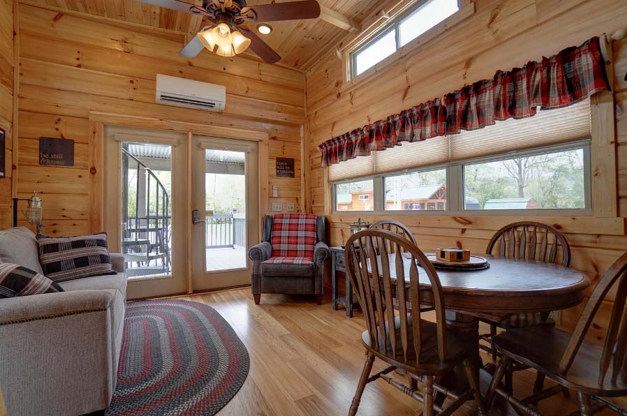Cabin interior with couch, ceiling fan, windows, chair, and dining area