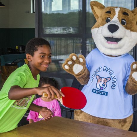 boy playing ping pong with Biscuit the camp mascot in the ultimate hangout at Great Escapes RV Resorts Bryan College Station